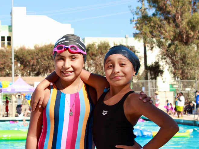 Two young girls in swim caps and goggles at a pool.